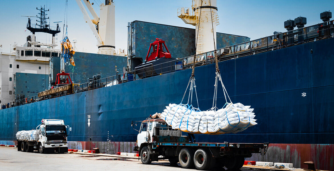 Theme picture: Ship crane lift-off slings of sugar bags cargo from truck and load into ship hold at seaport terminal for export.