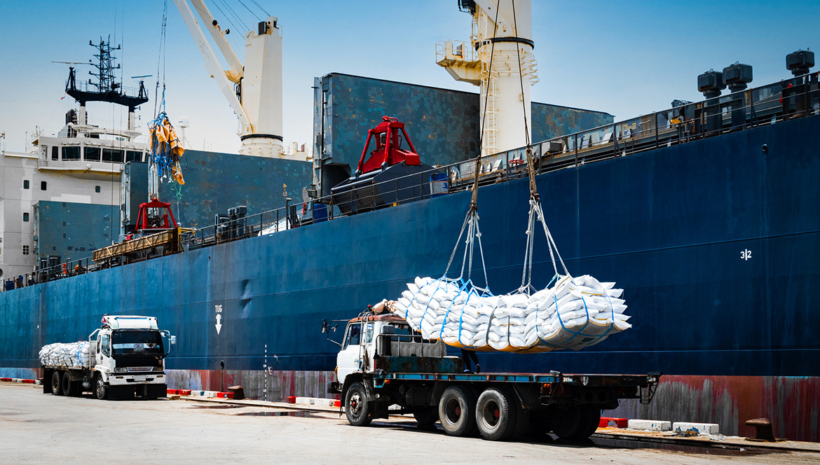 Theme picture: Ship crane lift-off slings of sugar bags cargo from truck and load into ship hold at seaport terminal for export.