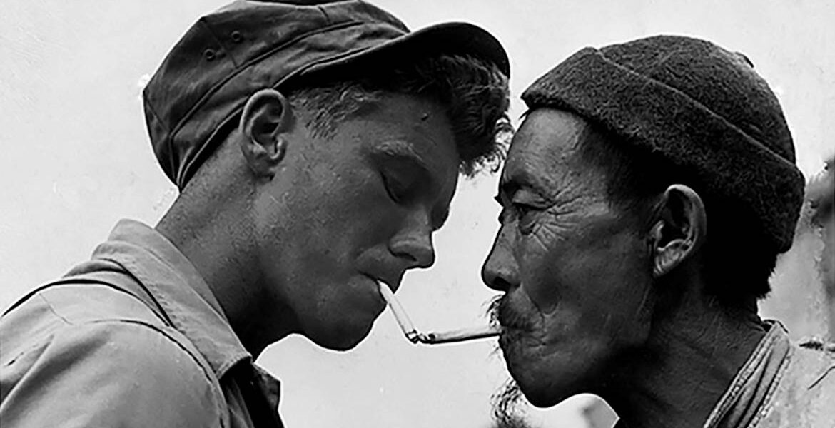Pausing on a street in bomb-shattered Tengchung, a Chinese civilian a U.S. Army sergeant exchange light for cigarettes, October 14, 1944.