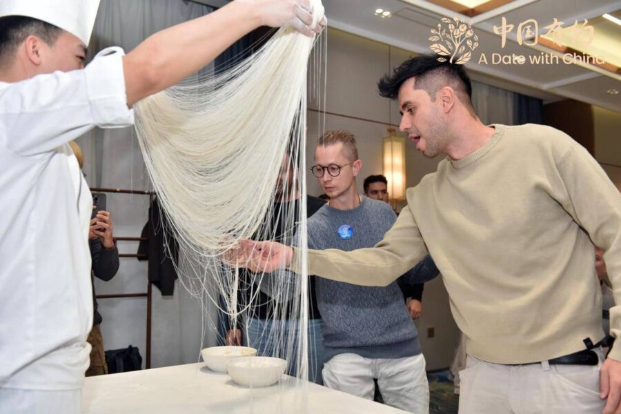 Utländska innehållsskapare undersöker nudlar som är tunna som hårstrån under en konstföreställning med Shanxi-nudlar i Taiyuan